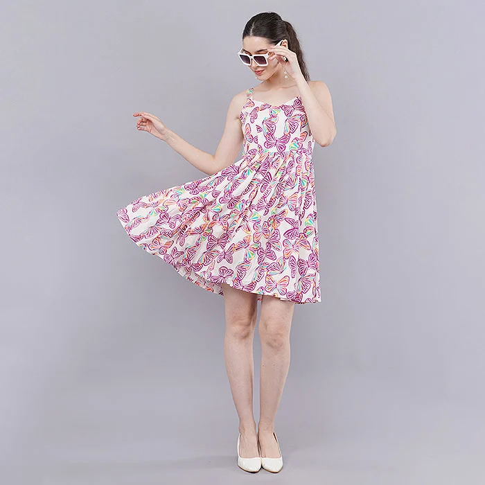 Three-quarter angle on-model photo of an Indian female model in a pink and white paisley print tiered strappy mini dress with sunglasses on her head and white heels, posed on a light grey seamless backdrop to show flare and fit