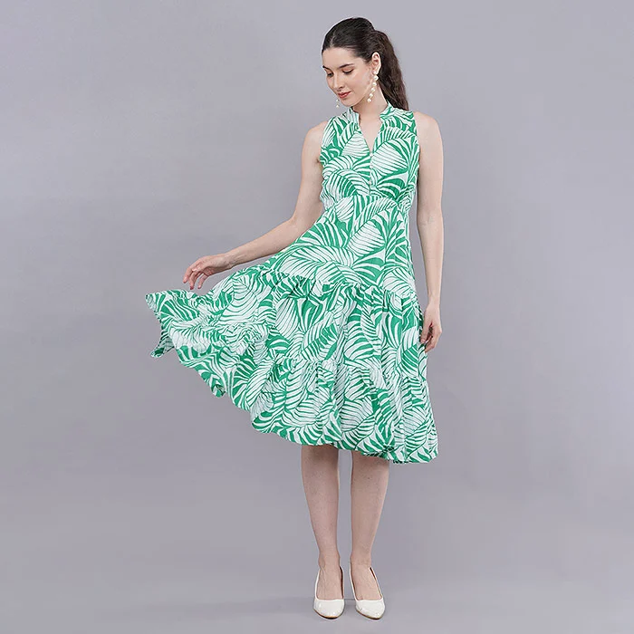 Indian female model in a green and white tropical leaf print sleeveless midi dress holding the flared skirt out, white heels, soft grey studio backdrop with even softbox light, an on-model fashion image for a clothing variation listing