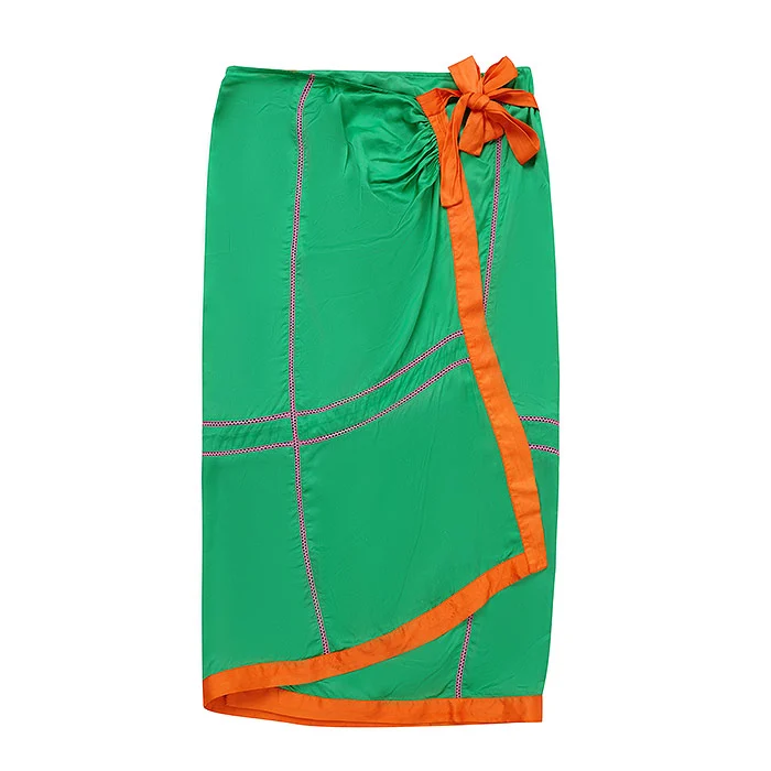 Kids flat lay photography of a green wrap skirt with orange piping and an orange fabric bow tie, laid flat on a pure white background with soft even lighting, a clean kids wear product image for a new Meesho supplier listing