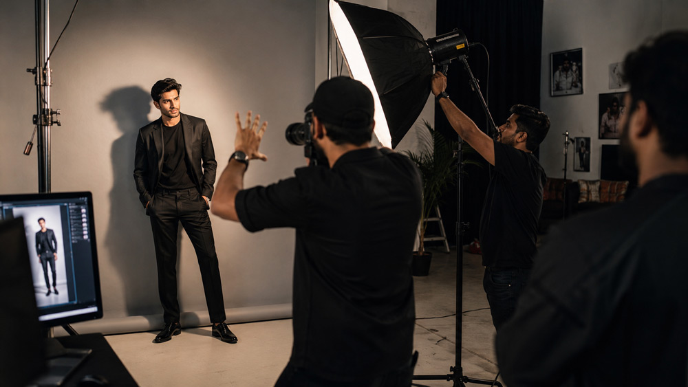 Behind-the-scenes shot of a Delhi fashion studio, photographer directing a model on set, lighting crew and softbox rigs visible, cinematic realism, warm bokeh, 4k detail, professional editorial production environment