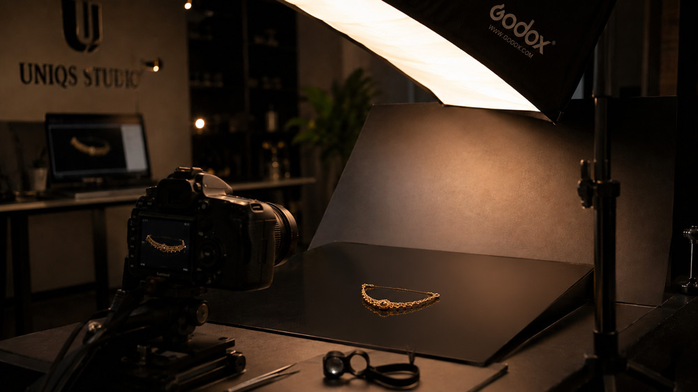Editorial hero shot of a Delhi NCR jewellery photography studio, macro focus on a 22K gold Indian necklace on dark reflective surface with warm champagne rim lighting and soft top-down softbox