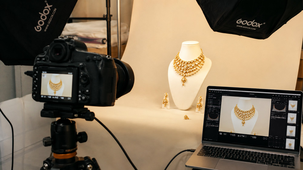 Premium e-commerce jewellery photography setup with softbox lighting and macro lens capturing a gold and diamond necklace on ivory backdrop by Uniqs Studio in Delhi NCR