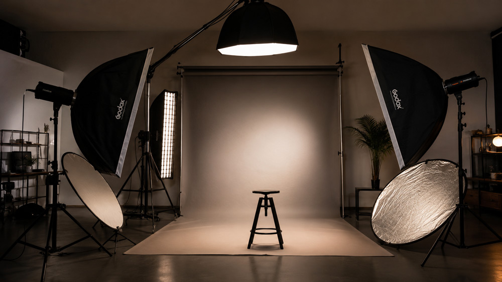 Professional fashion photography studio lighting setup with softboxes, reflectors and backdrop stand arranged for even catalogue lighting, moody cinematic atmosphere