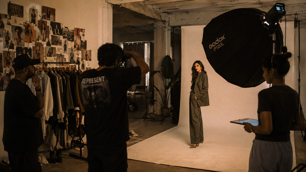 Behind the scenes of editorial fashion model photography shoot at Uniqs Studio Delhi NCR with softbox lighting mood board wardrobe rack and photographer directing model in cinematic warm tones documentary style 35mm lens film grain