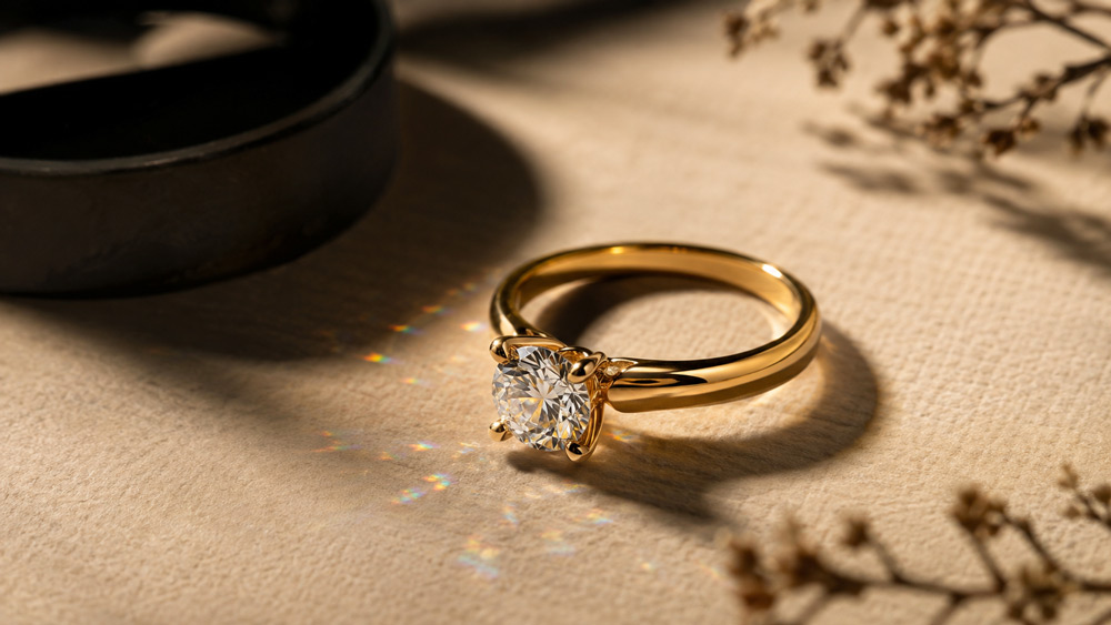 Ultra-cinematic macro photograph of a 22-karat gold diamond solitaire ring on warm ivory textured paper, editorial jewellery magazine styling, soft directional key light, shallow depth of field, 100mm macro lens aesthetic, gemstone sparkle with rainbow refraction, Vogue India cover quality, photorealistic 8K, warm ivory deep gold matte black palette